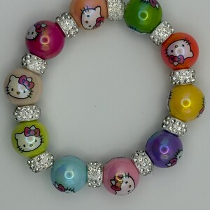 Pode incluir: Uma pulseira de contas coloridas com rostos de Hello Kitty em contas de várias cores. A pulseira inclui contas rosa, laranja, amarelas, verdes e azuis, separadas por espaçadores de strass prateados. Um acessório divertido.
