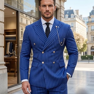 May include: A double-breasted blue suit with white pinstripes, featuring gold buttons, a white collared shirt, and a black tie. A silver lapel chain is attached to the jacket. The text Royal Creation Hub is visible on the storefront window.