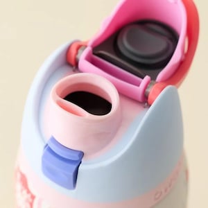 May include: Close-up of a pink and light blue water bottle with a floral design. The bottle has a pink flip-top lid and a blue locking mechanism. The interior of the bottle is black.