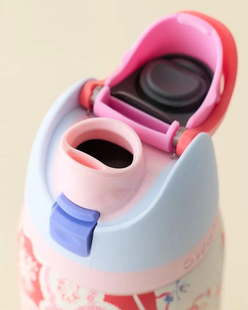 May include: Close-up of a pink and light blue water bottle with a floral design. The bottle has a pink flip-top lid and a blue locking mechanism. The interior of the bottle is black.