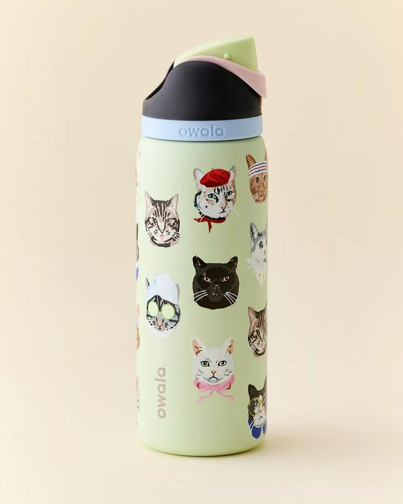 May include: A light green Owala water bottle featuring various cat faces with accessories. The bottle has a black and light green lid with a light blue band. The word "owala" is printed on the side.