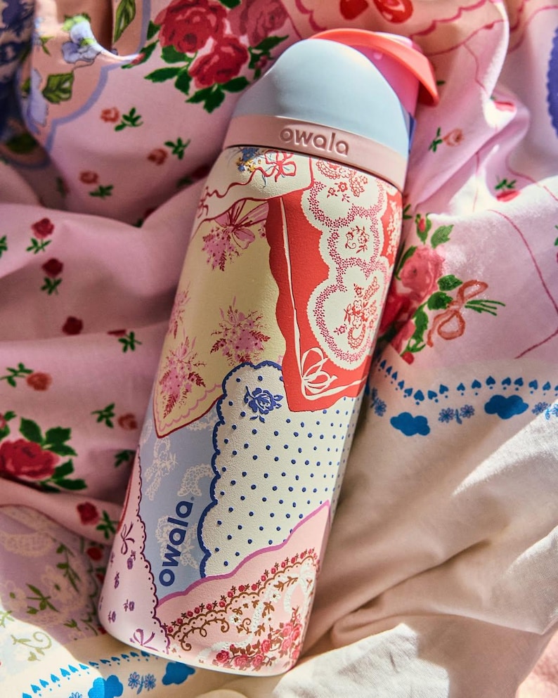 May include: A floral patterned water bottle with a light blue top and pink accents. The bottle features a variety of floral designs in pink, red, and blue. The brand name "owala" is printed on the bottle.