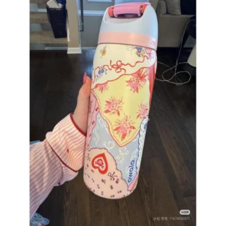 May include: A floral patterned water bottle with a pink and light blue lid. The bottle features a mix of pastel colors, including pink, yellow, and blue, with floral and heart designs. The word "owala" is printed on the side.