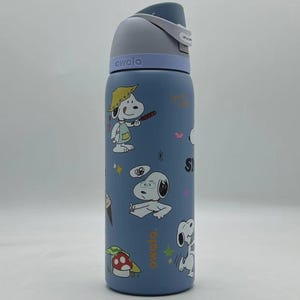 May include: A blue Owala water bottle featuring Snoopy and other Peanuts characters. The bottle has a gray lid and a white strap. The bottle is covered in cartoon illustrations of Snoopy in various poses, along with other graphics.