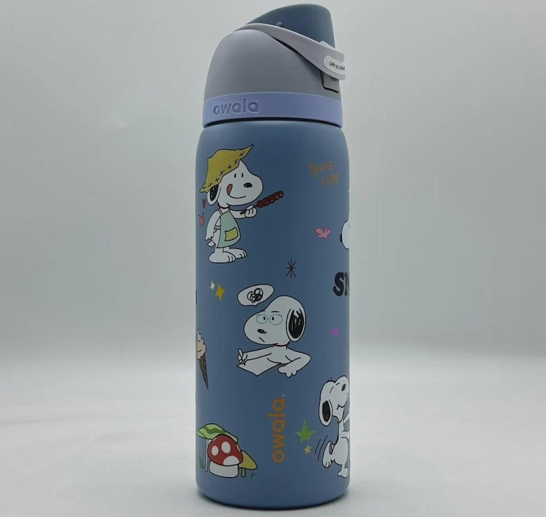 May include: A blue Owala water bottle featuring Snoopy and other Peanuts characters. The bottle has a gray lid and a white strap. The bottle is covered in cartoon illustrations of Snoopy in various poses, along with other graphics.