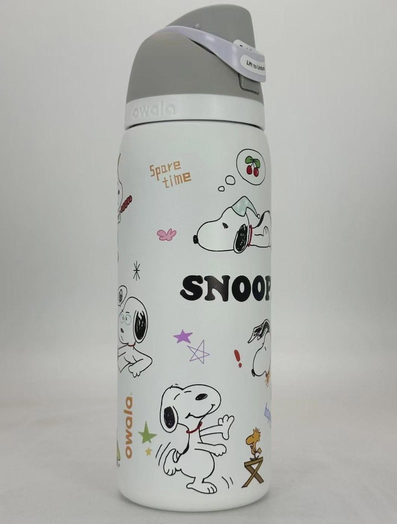 May include: White Owala water bottle featuring Snoopy illustrations and the word "SNOOP". The bottle has a gray lid with a white carrying strap. The words "Spare time" are also printed on the bottle.