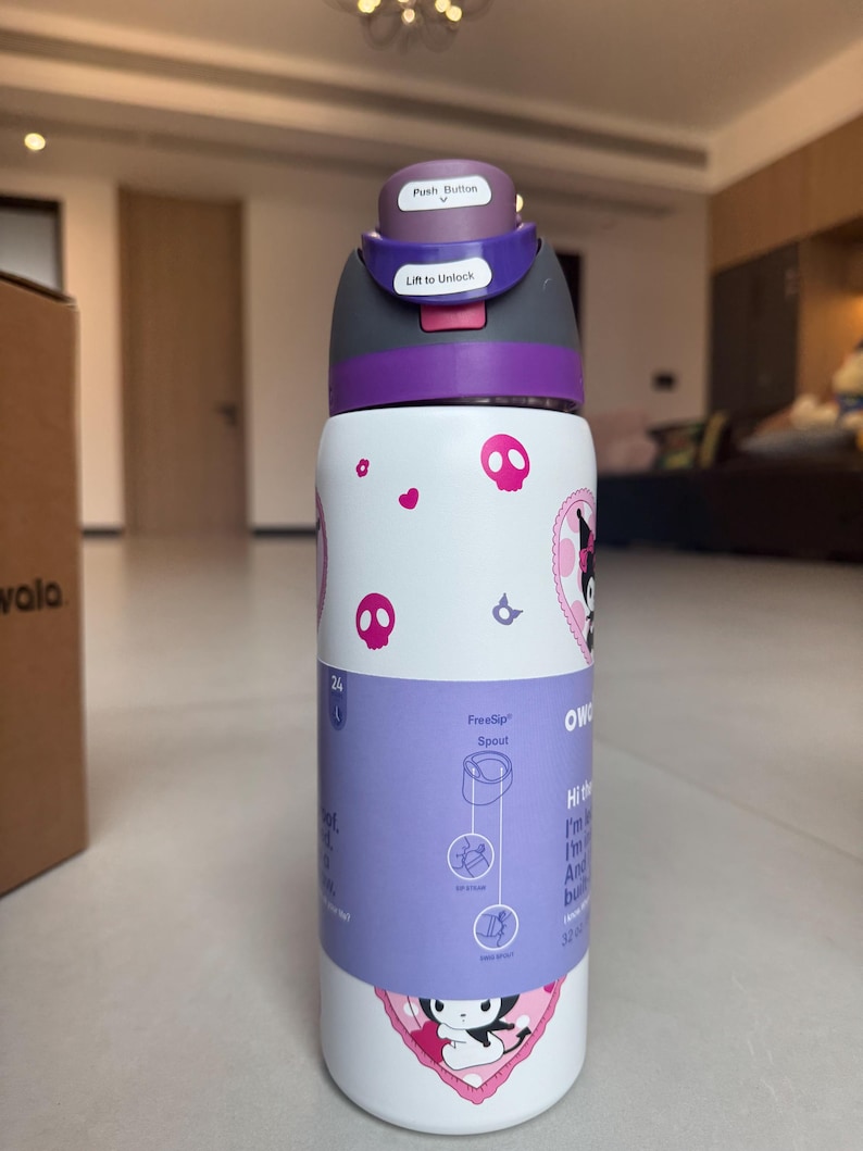 Puede incluir: Una botella de agua blanca y morada con un dise&ntilde;o de dibujos animados. La botella tiene una tapa con bot&oacute;n y una boquilla FreeSip. El dise&ntilde;o incluye calaveras rosas y un personaje de dibujos animados. La botella es de 946 ml.