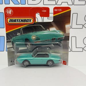Può includere: Un modellino Matchbox di un'auto sportiva Alfa Romeo color teal. L'auto è in una confezione di plastica trasparente con una carta rossa e gialla con il logo Matchbox e l'emblema Alfa Romeo. Il modello è lungo 7.6 cm.