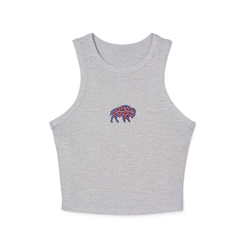 May include: A light gray crop top with a small embroidered buffalo design. The buffalo is filled with red and blue stars. The top has a rounded neckline and sleeveless design.