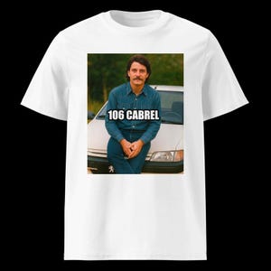 Puede incluir: Camiseta blanca con un gráfico de un hombre con camisa y vaqueros de mezclilla apoyado en un coche. El texto "106 CABREL" está impreso en el gráfico en blanco.