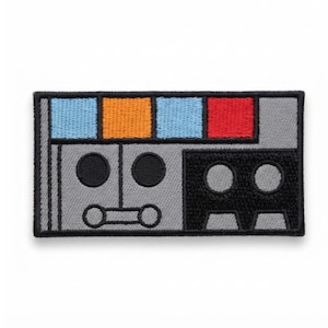 May include: A rectangular embroidered patch featuring a gray base with a black border. The top section displays four squares in light blue, orange, light blue, and red. The lower portion includes two black circles and a horizontal line with two circles.