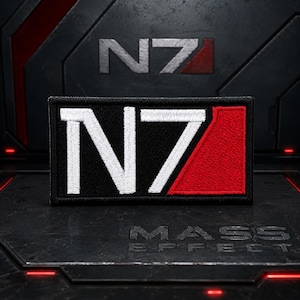 May include: A rectangular embroidered patch featuring the N7 logo. The design consists of a white letter N and the number 7, with a solid red diagonal stripe filling the upper right corner, all set against a black background with a black border.