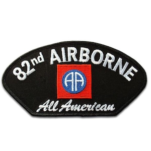 May include: A black embroidered patch with a curved top edge. It features the white text 82nd AIRBORNE at the top and All American at the bottom. In the centre is a red square containing a blue circle with the white letters AA inside the circle.