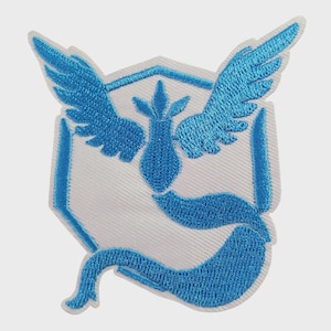 May include: An embroidered patch featuring a white shield shape with a bright blue stylized bird emblem. The bird has outstretched wings and a long tail that curves along the bottom edge of the shield, creating a detailed graphic design.