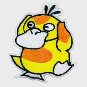 May include: An embroidered patch featuring a yellow, duck-like creature with a white bill, orange patches on its body, and three black tufts of hair on its head. The character has a black outline and a white border, depicted in a cartoon style.