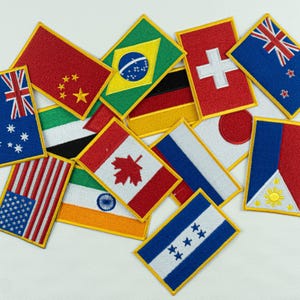May include: A collection of rectangular embroidered patches featuring various national flags, including those of the United States, Canada, Australia, Brazil, China, Switzerland, New Zealand, Japan, India, Germany, the Philippines, and Honduras.