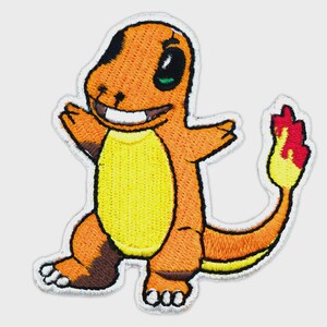 May include: An embroidered patch featuring a cartoon lizard character with orange skin, a yellow belly, and a long tail ending in a bright red and yellow flame. The character has a wide grin, white teeth, and dark eyes, outlined in white thread.