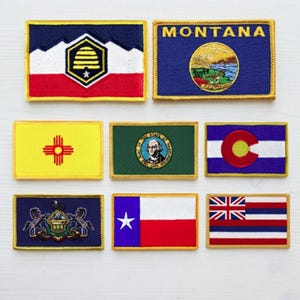 May include: A collection of eight rectangular embroidered patches featuring various United States state flags. The set includes designs for Utah, Montana, New Mexico, Washington, Colorado, Pennsylvania, Texas, and Hawaii, all with gold-colored borders.
