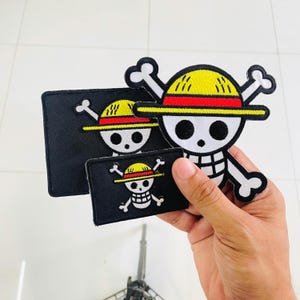 May include: Three embroidered patches featuring the One Piece skull and crossbones logo. One large die-cut patch shows a skull wearing a yellow straw hat with a red band. Two rectangular black patches feature the same skull and hat design.