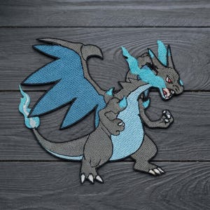May include: An embroidered patch featuring a stylized dragon creature with grey skin, large blue wings, and a blue flame-like mane. The creature has sharp claws, a pointed tail with a blue flame tip, and red eyes, rendered in detailed thread work.