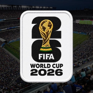 May include: A rectangular embroidered patch with a white border featuring the black text 26 and the FIFA World Cup 2026 logo. The design includes a gold and green trophy icon centered within the black numbers, set against a white background.