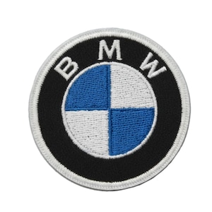 May include: A circular embroidered patch featuring the BMW logo. The design includes a black outer ring with the white letters B, M, and W, and a central circle divided into four quadrants of alternating blue and white colors with a white border.