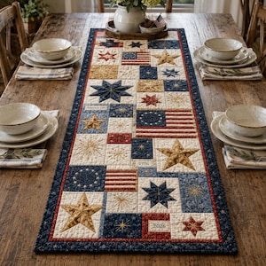 May include: A quilted table runner with a patriotic theme. The runner features a patchwork design with stars, stripes, and other patriotic symbols in red, white, blue, and gold. The text "America 250", "1776", and "2026" are visible.
