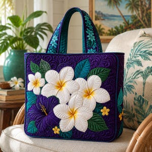 Puede incluir: Un bolso tote acolchado en morado oscuro, adornado con flores de frangipani blancas y amarillas, hojas verde azulado y un hibisco morado. Las asas son verde azulado con flores bordadas. El bolso está sobre una silla de mimbre.