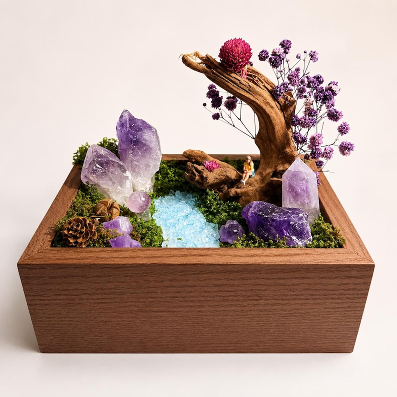 May include: A rectangular wooden box containing a miniature landscape with green moss, purple amethyst crystal clusters, a piece of driftwood, dried purple flowers, a small blue glass stream, and a tiny figurine sitting on the wood.