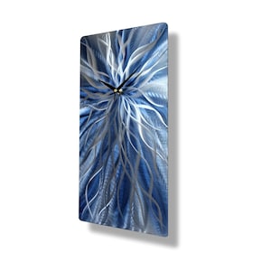 Puede incluir: Un reloj de pared rectangular con un diseño abstracto azul y plateado. La esfera del reloj presenta un aspecto texturizado y metálico con un patrón floral. Las manecillas del reloj son negras y el diseño es moderno.
