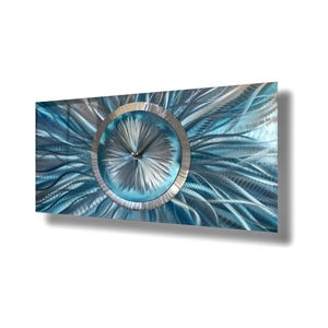 May include: A rectangular metal wall clock with a blue and silver color scheme. The clock face is circular with a silver frame and hands. The background features a textured, abstract design in shades of blue and silver.