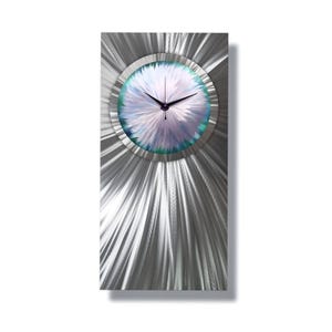 Puede incluir: Un reloj de pared moderno con acabado metálico plateado. La esfera del reloj presenta un diseño central con tonos blancos, azules y morados. Las manecillas del reloj son negras. El reloj es rectangular y tiene un diseño de rayos de sol.