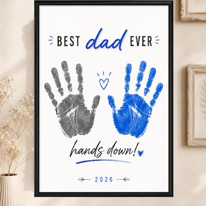 May include: A framed wall art print featuring the text BEST dad EVER and hands down! with a grey handprint and a blue handprint in the center. A small blue heart and the year 2026 are printed below the handprints on a white background.