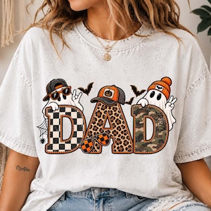 Könnte beinhalten: Ein weißes Acid-Wash-T-Shirt mit einer Grafik des Wortes DAD in großen Buchstaben. Die Buchstaben sind mit schwarz-weißem Schachbrettmuster, Leopardenmuster und Camouflage gefüllt. Drei Geister mit Hüten und Sonnenbrillen sind darüber abgebildet.