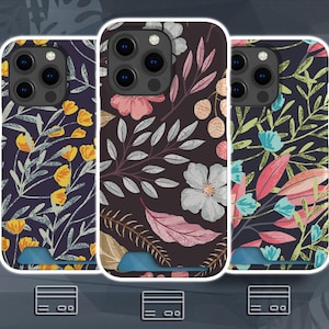 Puede incluir: Tres fundas para smartphone con estampados florales sobre fondos oscuros. La funda izquierda tiene flores amarillas, la central flores rosas y blancas, y la derecha hojas azules y rosas. Cada funda incluye una ranura para tarjetas en la parte inferior.