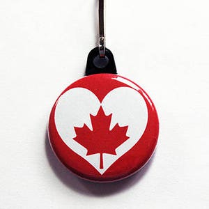 Könnte beinhalten: Ein runder, roter Knopf mit einem weißen Herz und einem roten Ahornblatt in der Mitte. Der Knopf hat einen silberfarbenen Clip. Das Design ist ein patriotisches Symbol Kanadas.