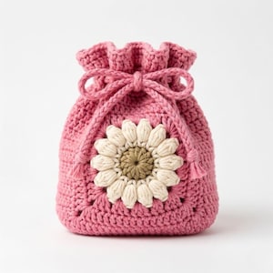 May include: A pink crocheted drawstring bag with a large, cream and brown sunflower applique. The bag has a ruffled top and a matching pink drawstring closure. The bag is handmade and suitable for small items.