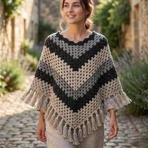 May include: A handmade crochet poncho in a chevron pattern, featuring shades of gray, black, and beige. The poncho has a fringed hemline and is made of soft yarn. This cozy garment is perfect for cool weather.