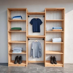 May include: A wooden wardrobe with multiple shelves and hanging rods. The shelves display folded clothes in various colors, including blue, green, and white. A navy blue t-shirt and a gray long-sleeve shirt hang on the rods. Dark brown boots are placed on the bottom shelves.
