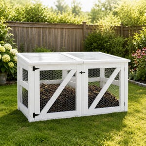 May include: A white wooden compost bin featuring two separate compartments with hinged lids and wire mesh sides. The structure has a slanted top design, black metal hinges, and a latch, containing dark organic matter within each section.