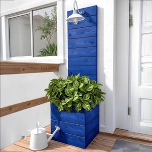 May include: A vibrant blue wooden planter box filled with lush green plants. The planter is mounted on a wall and features a built-in light fixture. A white watering can sits nearby, adding a touch of functionality to the outdoor decor.