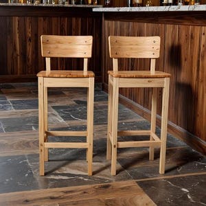 Könnte beinhalten: Zwei Barhocker aus Holz mit hellen Rahmen und Sitzflächen und Rückenlehnen aus Naturholz. Die Hocker haben ein schlichtes, klassisches Design mit einer rechteckigen Sitzfläche und einer mit sichtbaren Schrauben befestigten Rückenlehne. Die Hocker stehen vor einer Holzbar.