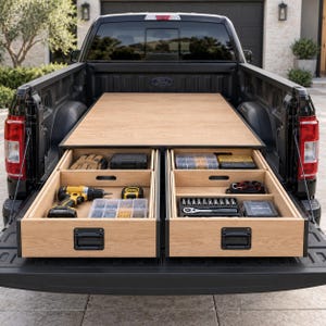May include: A black Ford pickup truck bed featuring a custom wooden storage system with two large, pull-out drawers. The drawers are organised with various tools, including a yellow power drill, a tape measure, socket sets, and hardware containers.