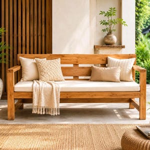May include: A wooden bench with a light-colored seat cushion, featuring two square pillows, one rectangular pillow, and a cream-colored throw blanket with fringe draped over the front. The bench has a slatted backrest and straight armrests.