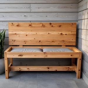 May include: A wooden bench with a backrest and two gray cushions. The bench is made of light-colored wood and has a simple, modern design. The bench is approximately 60 inches long and 24 inches deep.