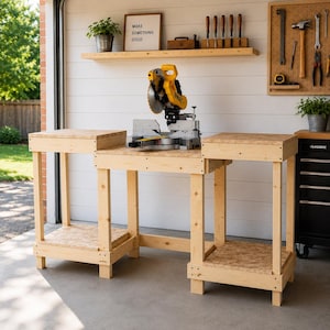 Op de afbeelding: Een werkplaatsopstelling met een gele en zilveren verstekzaag op een houten werkbank. De werkbank heeft twee bijzettafels. Een bord aan de muur leest "MAKE SOMETHING GOOD". Gereedschap en planten zijn zichtbaar op de achtergrond.
