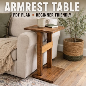 May include: A brown wooden armrest table with a square top and a vertical support base. The text ARMREST TABLE PDF PLAN BEGINNER FRIENDLY is displayed at the top. A ceramic mug and a small book are placed on the surface of the wooden table.
