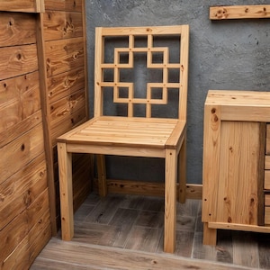 May include: A light-colored wooden chair with a geometric design on the back. The chair is made of natural wood and has a slatted seat. The chair is part of a set that includes a cabinet and wooden paneling.