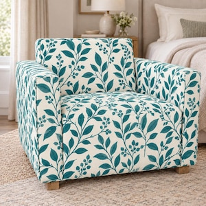 May include: An armchair upholstered in a cream-coloured fabric featuring a repeating pattern of teal green leaves and small berries. The chair has a square backrest, two wide armrests, a deep seat cushion, and short, light-coloured wooden legs.
