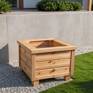 May include: A square wooden planter box with a natural finish. The box is constructed from horizontal wooden planks and sits on four short legs. The planter is empty and ready for plants. The background includes a concrete wall, green grass, and small white stones.
